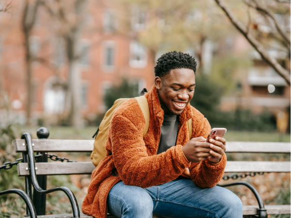 Man sits on a park bench smiling at his phone to illustrate sharing an Instagram post to Instagram Stories.