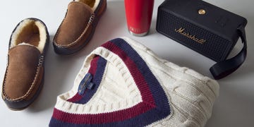 a pair of overland men's brown slippers, a brooks brothers cream colored tennis sweater with red and blue striped v neck collar, marshall middleton ii portable bluetooth speaker in black, and a red yeti rambler tumbler
