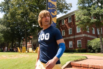 glen powell as chad powers, a man wears athletic clothing outdoors on a college campus
