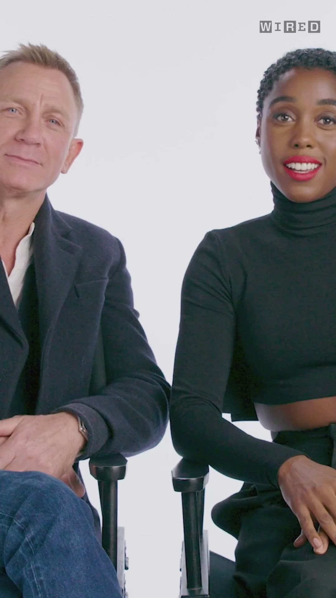 This may contain: two people sitting next to each other in front of a white background and one person is talking