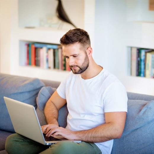 Mann mit Laptop auf einer Couch.