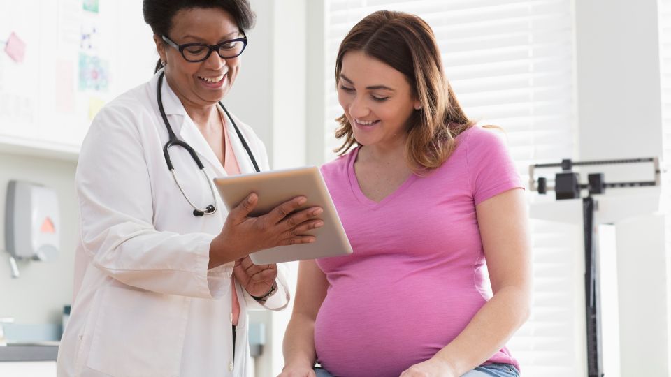 Pregnant person and doctor smiling Pregnant person and doctor smiling, looking at a tablet in a healthcare office.