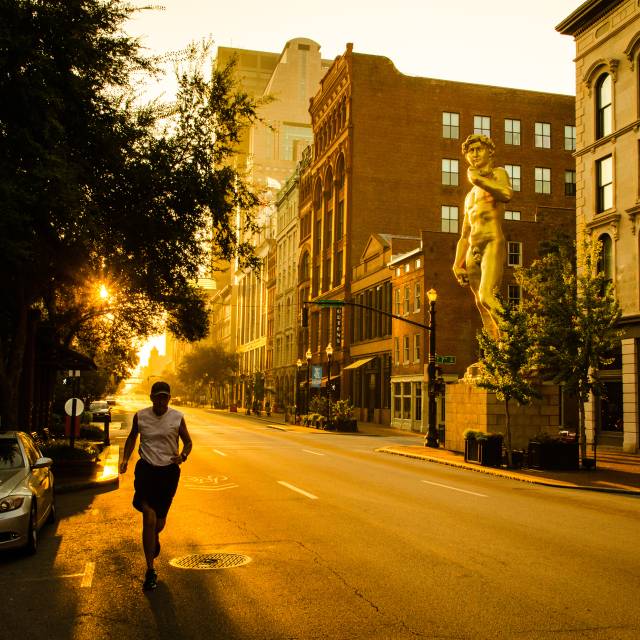 A man jogs down Main Street at sunrise. In the background is a 30-foot tall gold replica of the Statue of David and hotels.