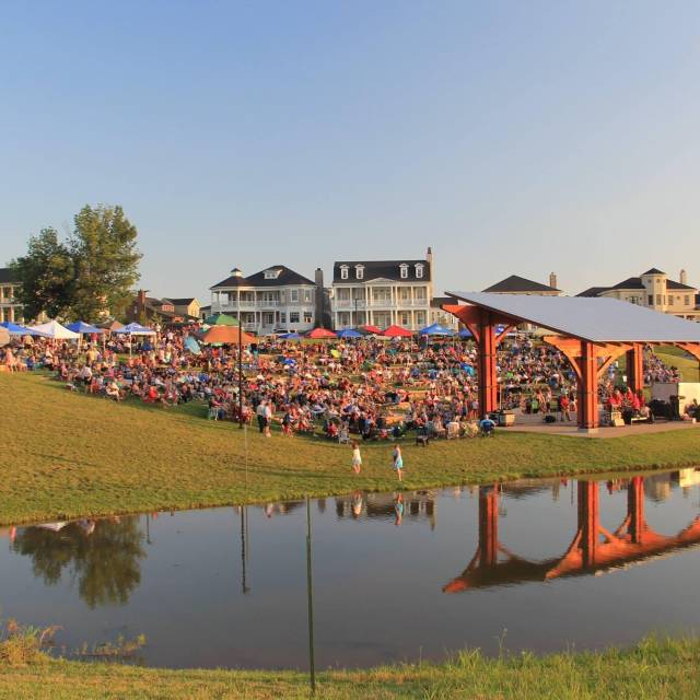 Daytime - a pond in the foreground with a full amphitheater behind and a concert playing.