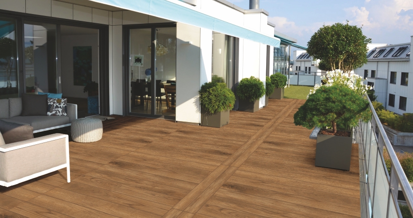 Modern outdoor terrace with wood flooring tile, potted plants, and seating area by glass doors.