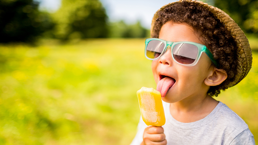 SupplyOne Young boy wearing a hat and sunglasses, licking a popsicle